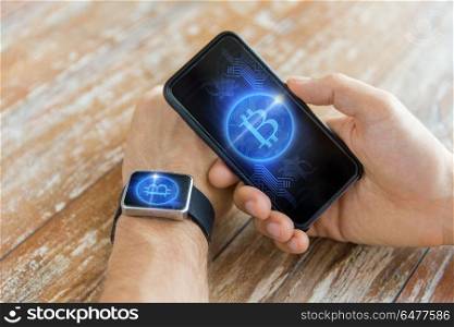 business, technology and cryptocurrency concept - close up of male hand holding smartphone and wearing smart watch with bitcoin on screen. close up of bitcoin on smartphone and smart watch. close up of bitcoin on smartphone and smart watch