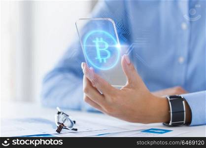 business, technology and cryptocurrency concept - close up of woman hand holding and showing transparent smartphone with bitcoin on screen. close up of bitcoin on transparent smartphone