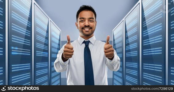 business, technology and data concept - smiling indian businessman in shirt with tie showing thumbs up over server room background. businessman showing thumbs up in server room