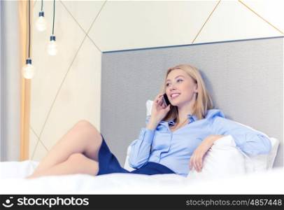 business, technology and hotel concept - happy businesswoman with smartphone lying in hotel in bed