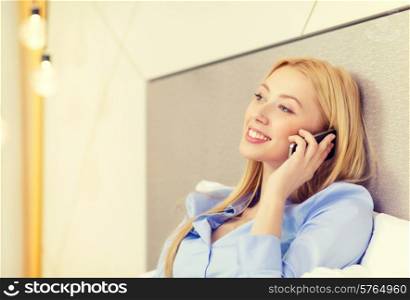 business, technology and hotel concept - happy businesswoman with smartphone lying in hotel in bed