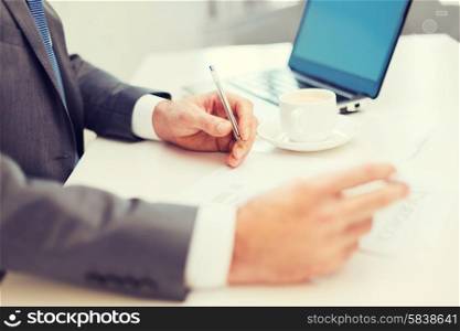 business, technology and internet concept - close up of man hands with contract and pen, coffee and laptop computer
