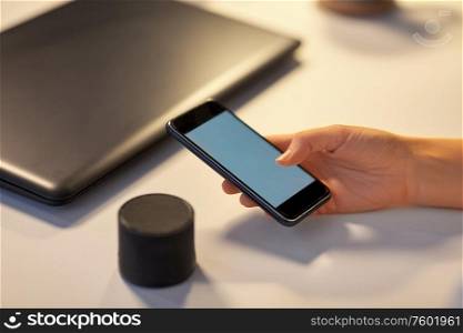 business, technology and internet of things concept - hand with smartphone and smart speaker at night office. hand with smartphone and smart speaker at office