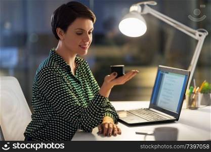 business, technology and internet of things concept - happy businesswoman using smart speaker at night office. businesswoman using smart speaker at night office