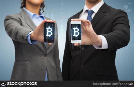 business, technology and internetconcept - businessman and businesswoman with bitcoin sign on smartphone screens
