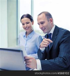 business, technology and office concept - businessman and businesswoman with laptop computer and papers having discussion in office. businessman and businesswoman having discussion