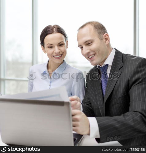 business, technology and office concept - businessman and businesswoman with laptop computer and papers having discussion in office