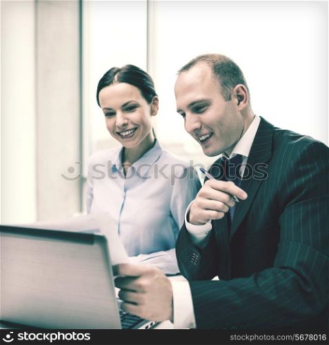 business, technology and office concept - businessman and businesswoman with laptop computer and papers having discussion in office