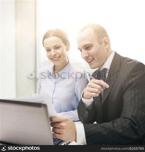 business, technology and office concept - businessman and businesswoman with laptop computer and papers having discussion in office