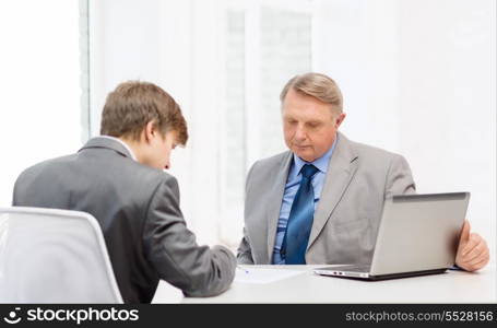 business, technology and office concept - older man and young man signing papers in office