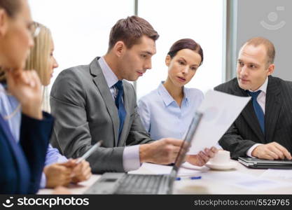 business, technology and office concept - serious business team with laptop computers, documents and coffee having discussion in office