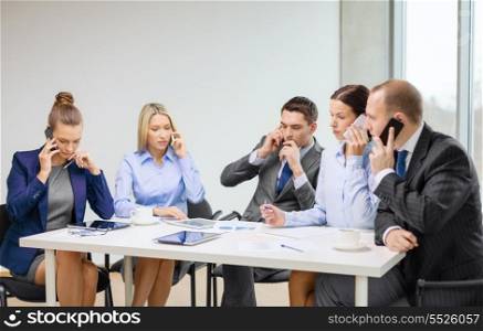 business, technology and office concept - serious business team with smartphones making calls in office