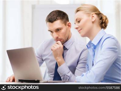business, technology and office concept - serious businessman and businesswoman with laptop computer at office
