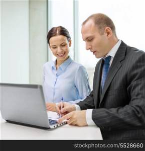 business, technology and office concept - smiling business team with laptop computer and documents having discussion in office