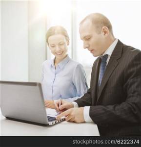 business, technology and office concept - smiling business team with laptop computer and documents having discussion in office