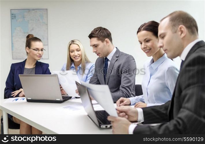 business, technology and office concept - smiling business team with laptop computers and documents having discussion in office