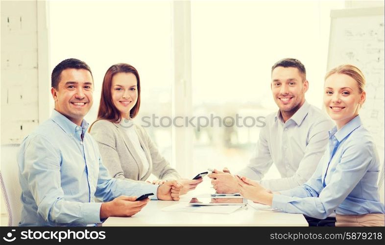 business, technology and office concept - smiling business team with smartphones having meeting in office