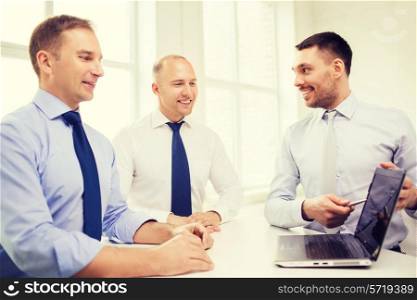 business, technology and office concept - smiling businessmen with laptop computer and papers having discussion in office
