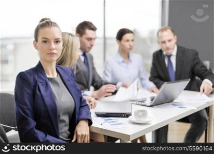 business, technology and office concept - smiling businesswoman in office with team on the back
