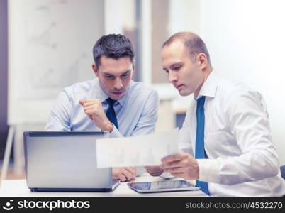 business, technology and office concept - two businessmen with laptop, tablet pc computer and papers having discussion in office