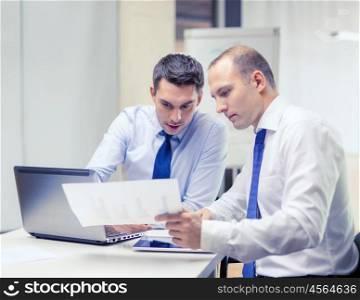 business, technology and office concept - two businessmen with laptop, tablet pc computer and papers having discussion in office