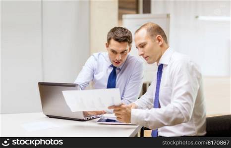 business, technology and office concept - two businessmen with laptop, tablet pc computer and papers having discussion in office