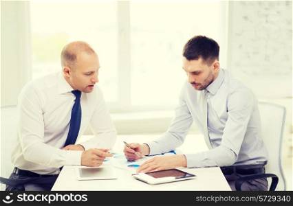 business, technology and office concept - two serious businessmen with tablet pc computers and files in office