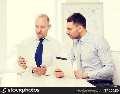 business, technology and office concept - two serious businessmen with tablet pc computers in office