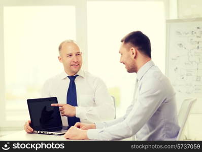 business, technology and office concept - two smiling businessmen with laptop having presentation in office