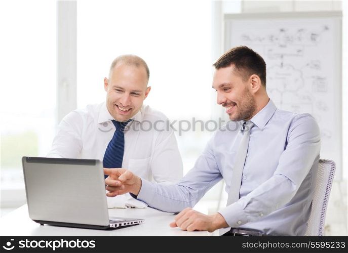 business, technology and office concept - two smiling businessmen with laptop in office