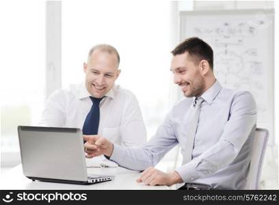 business, technology and office concept - two smiling businessmen with laptop in office