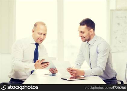 business, technology and office concept - two smiling businessmen with tablet pc computers and files in office