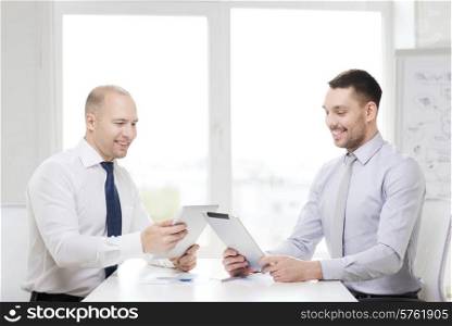 business, technology and office concept - two smiling businessmen with tablet pc computers and files in office