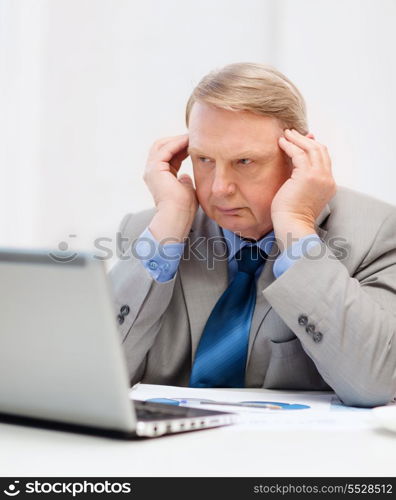 business, technology and office concept - upset older businessman with laptop and charts in office