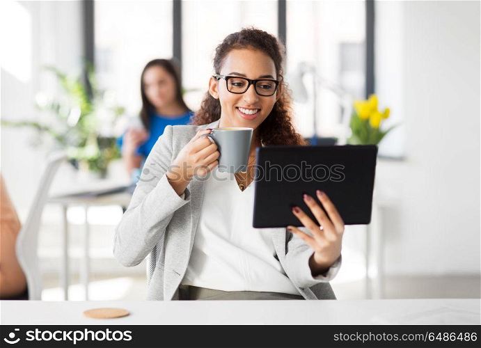 business, technology and people concept - african american businesswoman with tablet pc computer drinking coffee at office. businesswoman with tablet pc and coffee at office. businesswoman with tablet pc and coffee at office
