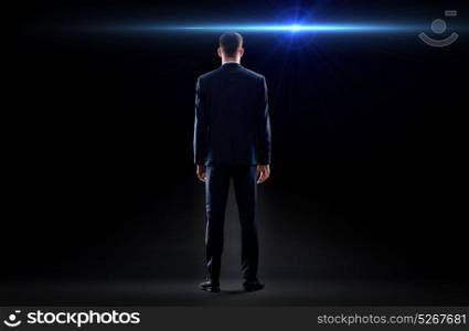 business, technology and people concept - businessman in suit over black background from back with laser light ray. businessman in suit from back with laser light