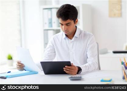 business, technology and people concept - businessman working with tablet pc computer and papers at office. businessman with tablet pc and papers at office