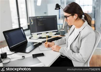 business, technology and people concept - businesswoman in earphones with notebook and computers working at office. businesswoman with notebook working at office