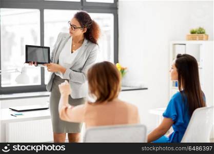business, technology and people concept - businesswoman showing tablet pc computer to female team at office. woman showing tablet pc to business team at office. woman showing tablet pc to business team at office