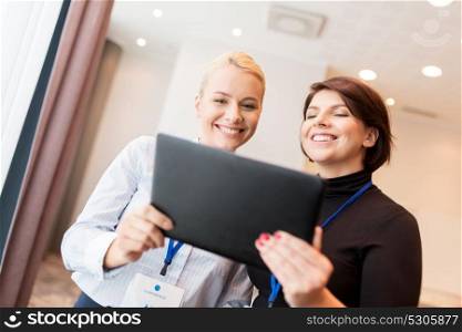 business, technology and people concept - businesswomen with tablet pc computer and conference badges. businesswomen with tablet pc and conference badges