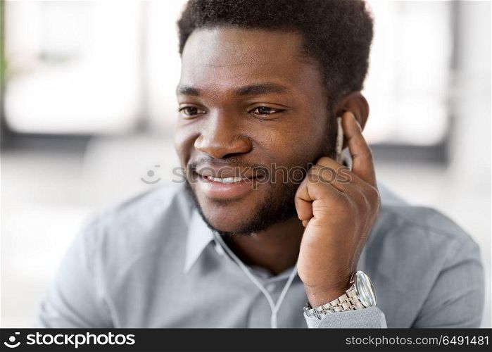 business, technology and people concept - close up of happy african american man with earphones listening to music at office. close up of man with earphones listening to music. close up of man with earphones listening to music