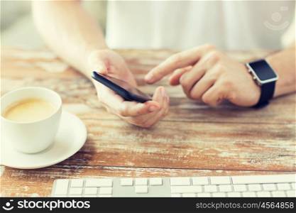 business, technology and people concept - close up of male hand holding smart phone and wearing watch with coffee and keyboard at wooden table