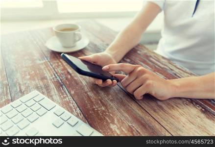 business, technology and people concept - close up of male hand holding smart phone with coffee and keyboard at wooden table