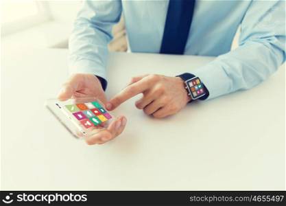 business, technology and people concept - close up of male hand holding and showing transparent smart phone and watch at office with menu icons on screen