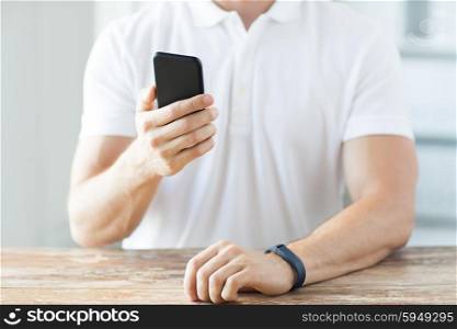 business, technology and people concept - close up of male hand holding smart phone and wearing heart-rate watch at home