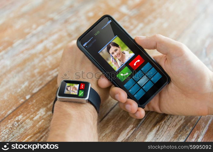 business, technology and people concept - close up of male hand holding smart phone and wearing smart watch with incoming call interface on screen