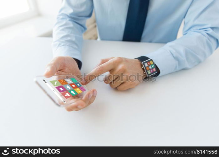 business, technology and people concept - close up of male hand holding and showing transparent smart phone and watch at office with menu icons on screen