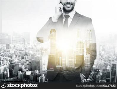 business, technology and people concept - close up of smiling businessman calling on smartphone over city buildings and double exposure effect. close up of businessman calling on smartphone