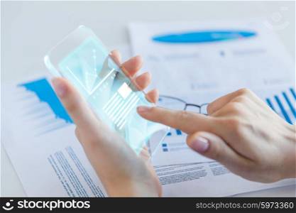 business, technology and people concept - close up of woman hand holding and showing transparent smartphone with chart on screen at office
