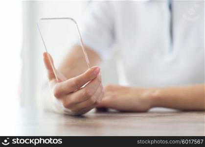 business, technology and people concept - close up of woman hand holding and showing transparent smartphone at home